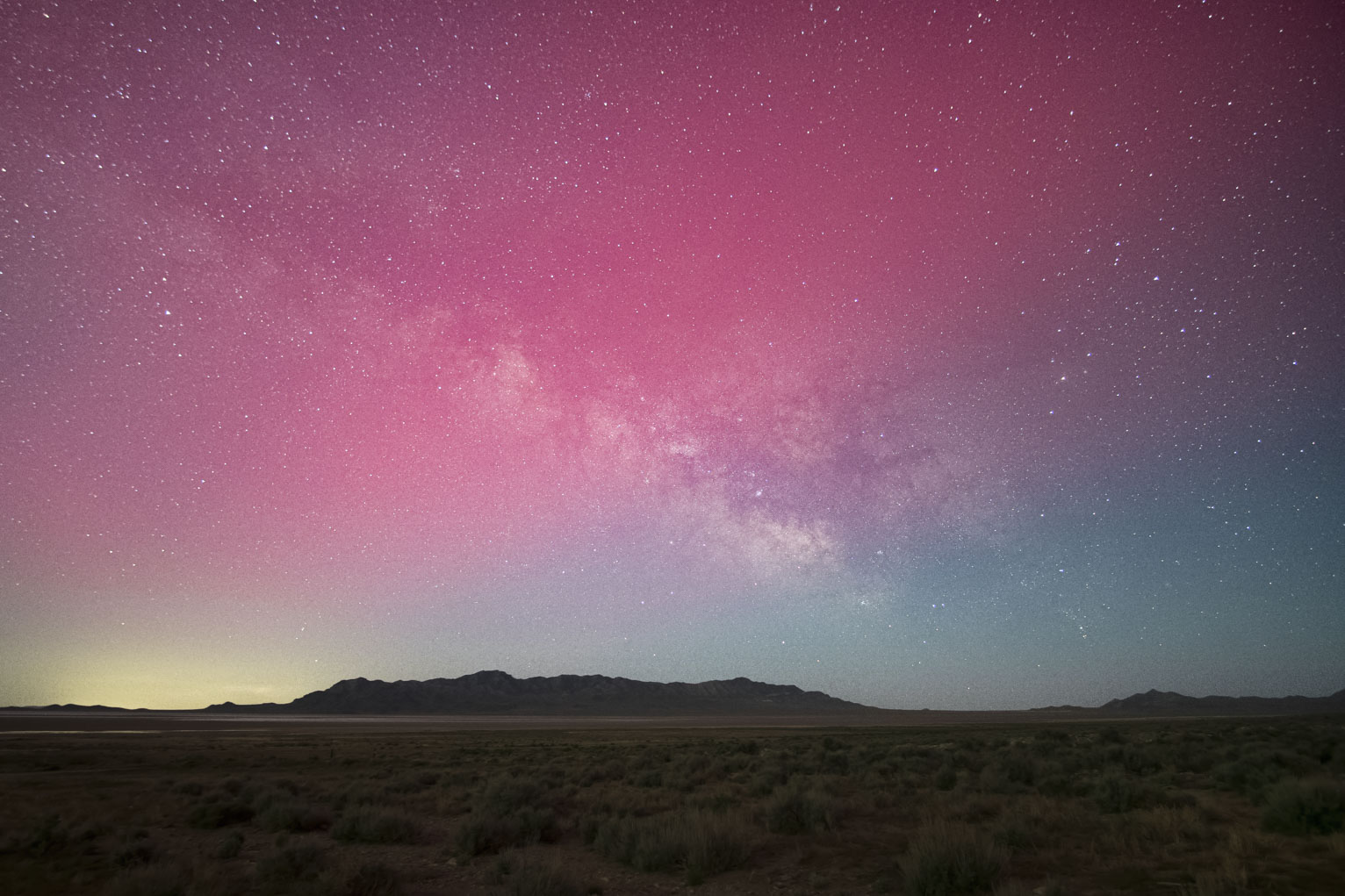 The pink glow of aurora slices through the milky way forming an X